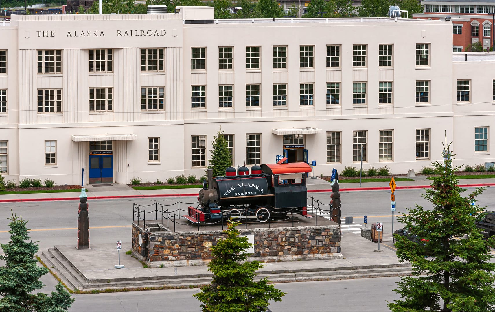Closeup, long white stone Alaska Railroad Depot Building with old train engine on display up front