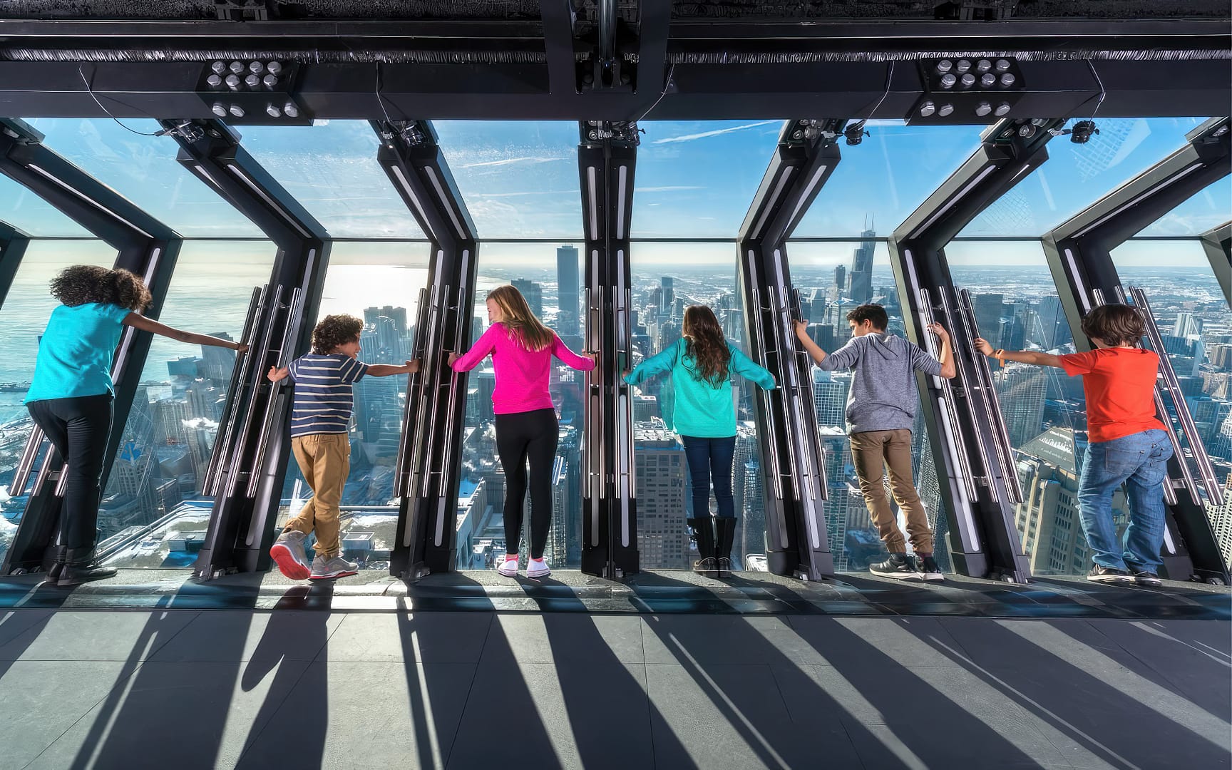 Six people view a cityscape from the 360 Chicago Observation Deck on a sunny day