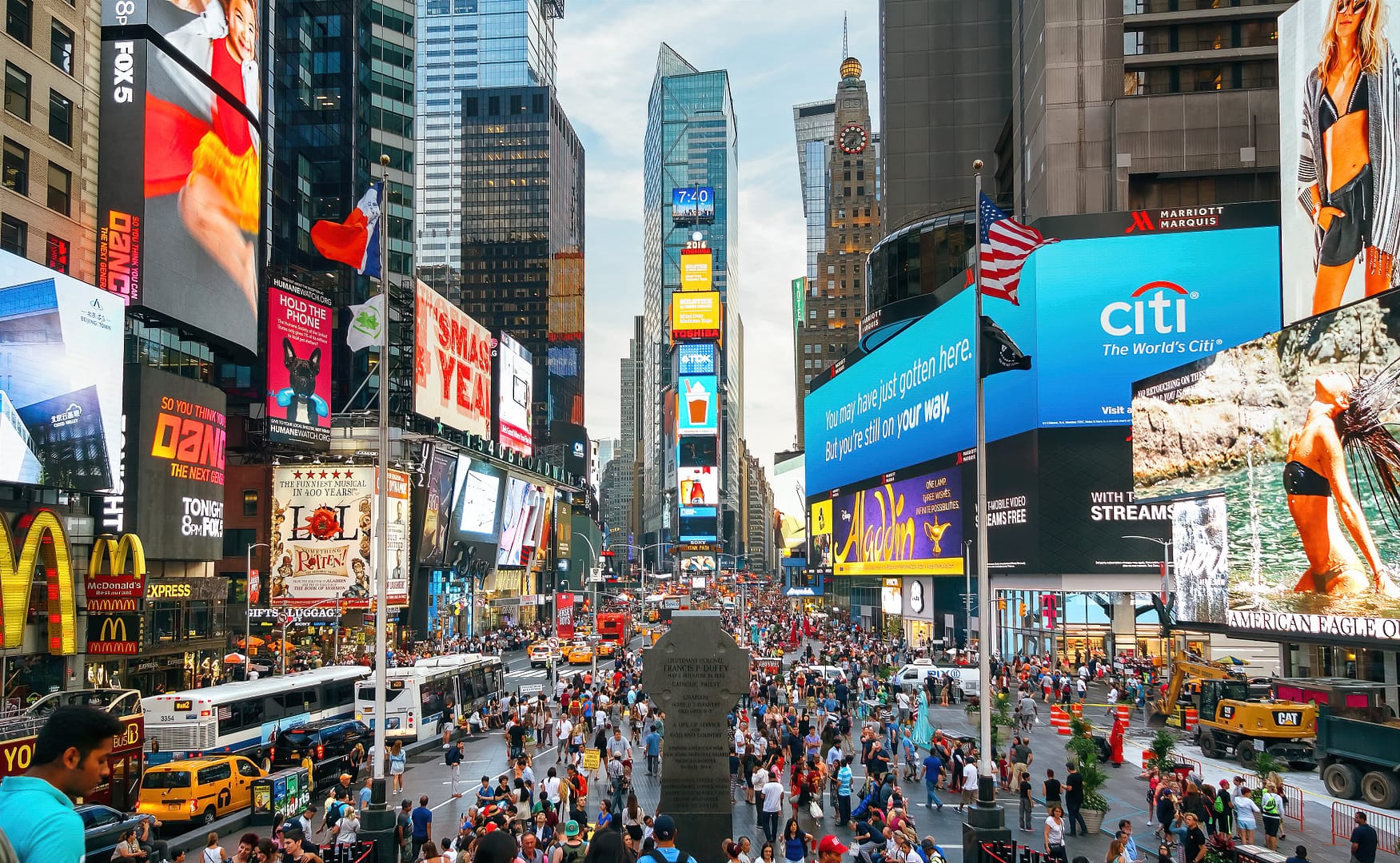 Crowded Times Square with people, large screen advertisements, and busy traffic on a sunny day