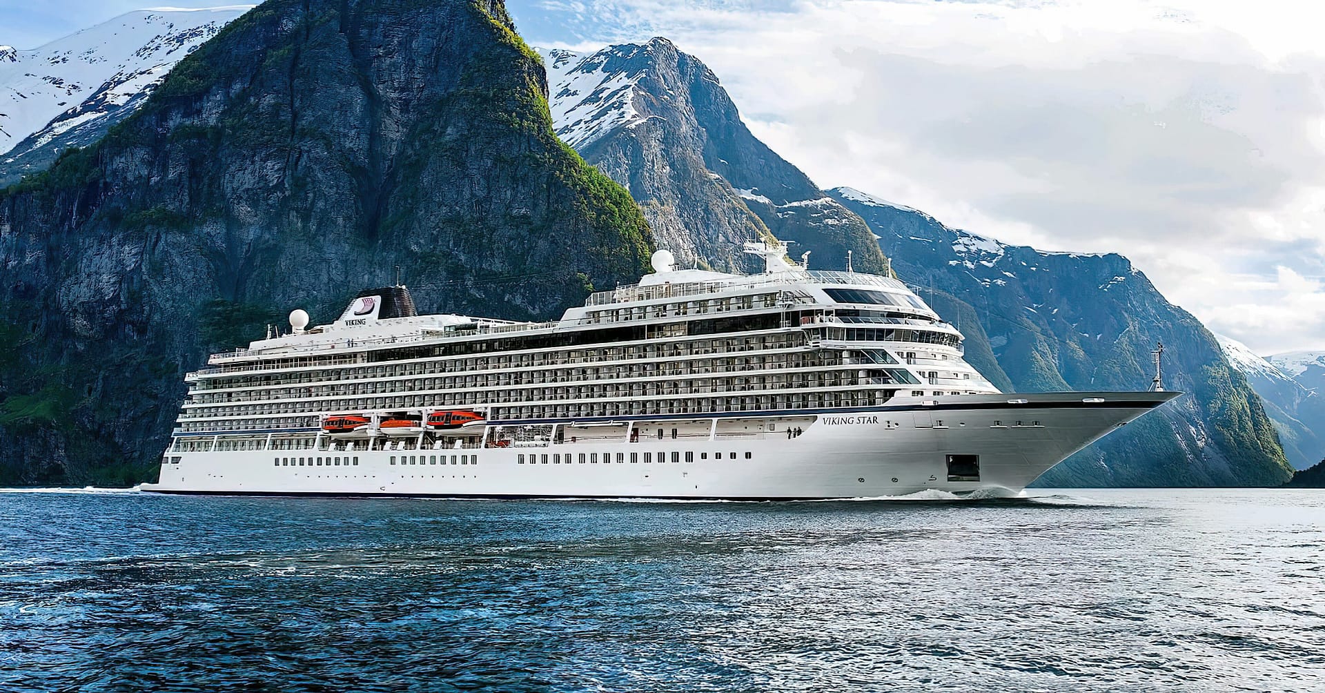 A large Viking Ocean Cruises ship sailing in a fjord with towering mountain cliffs on either side