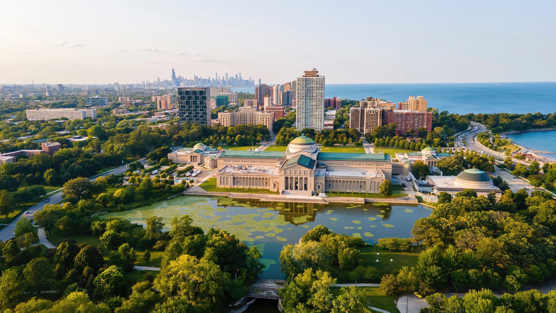 Aerial view of the Museum of Science and Industry in Chicago with surrounding greenery and distant city skyline