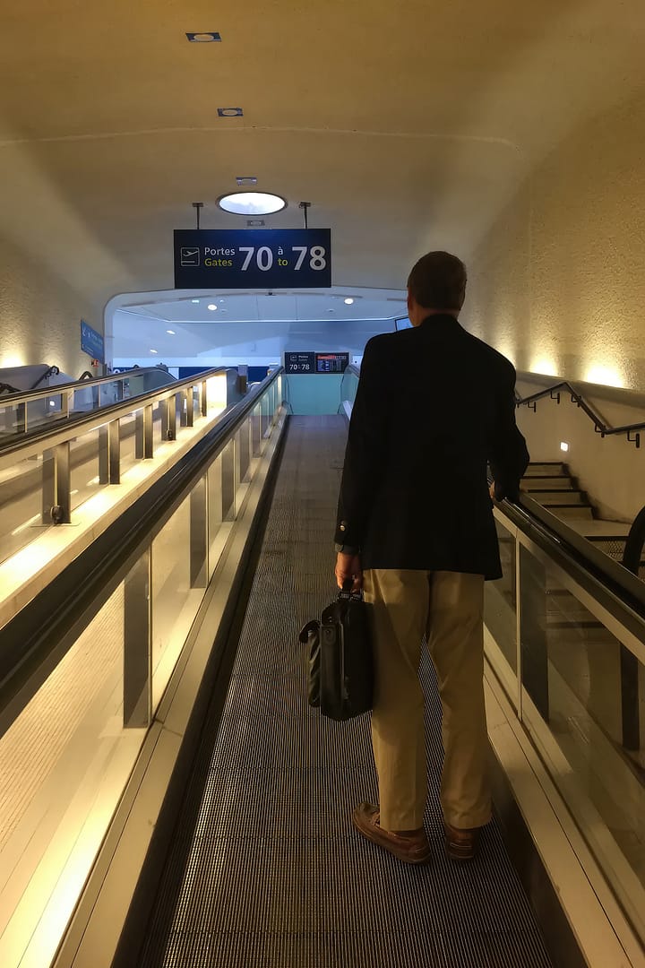 A male traveler standing on an escalator while holding a briefcase at an airport