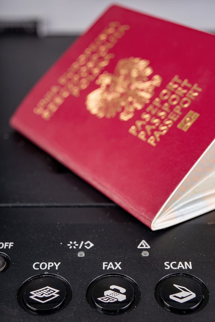 A red and gold Polish passport rests on a photocopier control panel featuring buttons labeled "COPY", "FAX" and "SCAN"