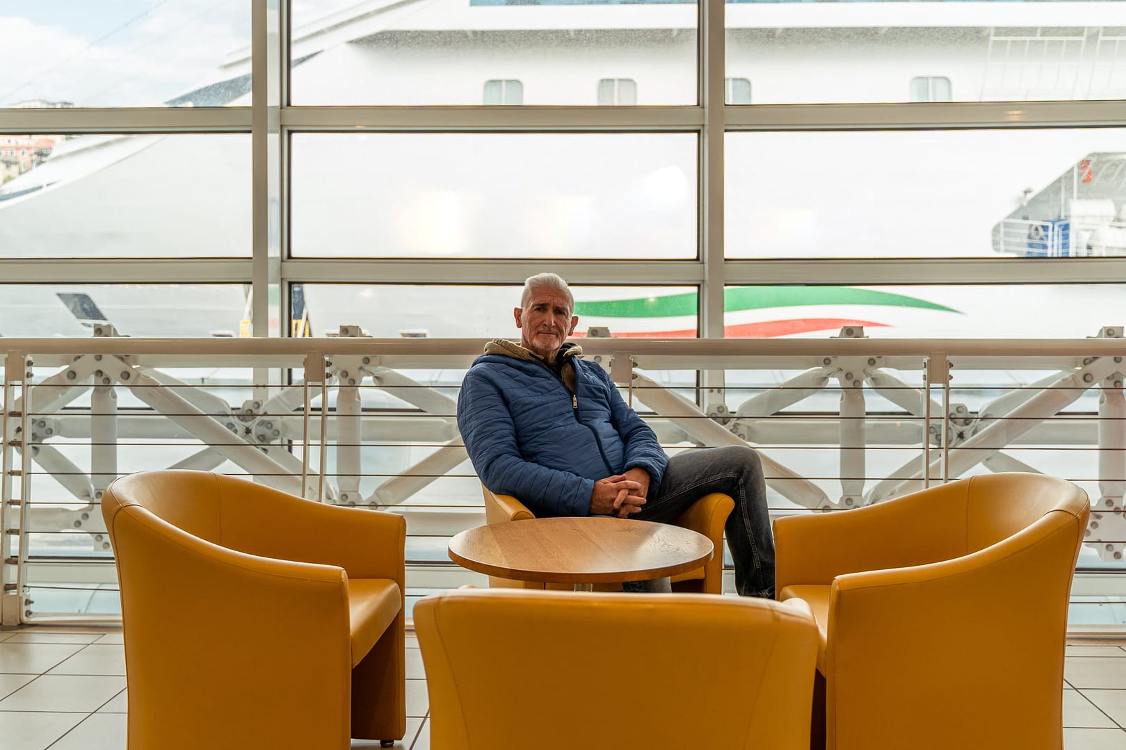 Middle aged man sitting in waiting room at port. He is a happy tourist traveling with cruise ship