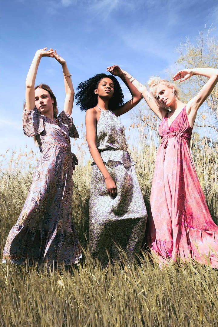 Three ladies in stylish dresses, standing gracefully in a scenic field