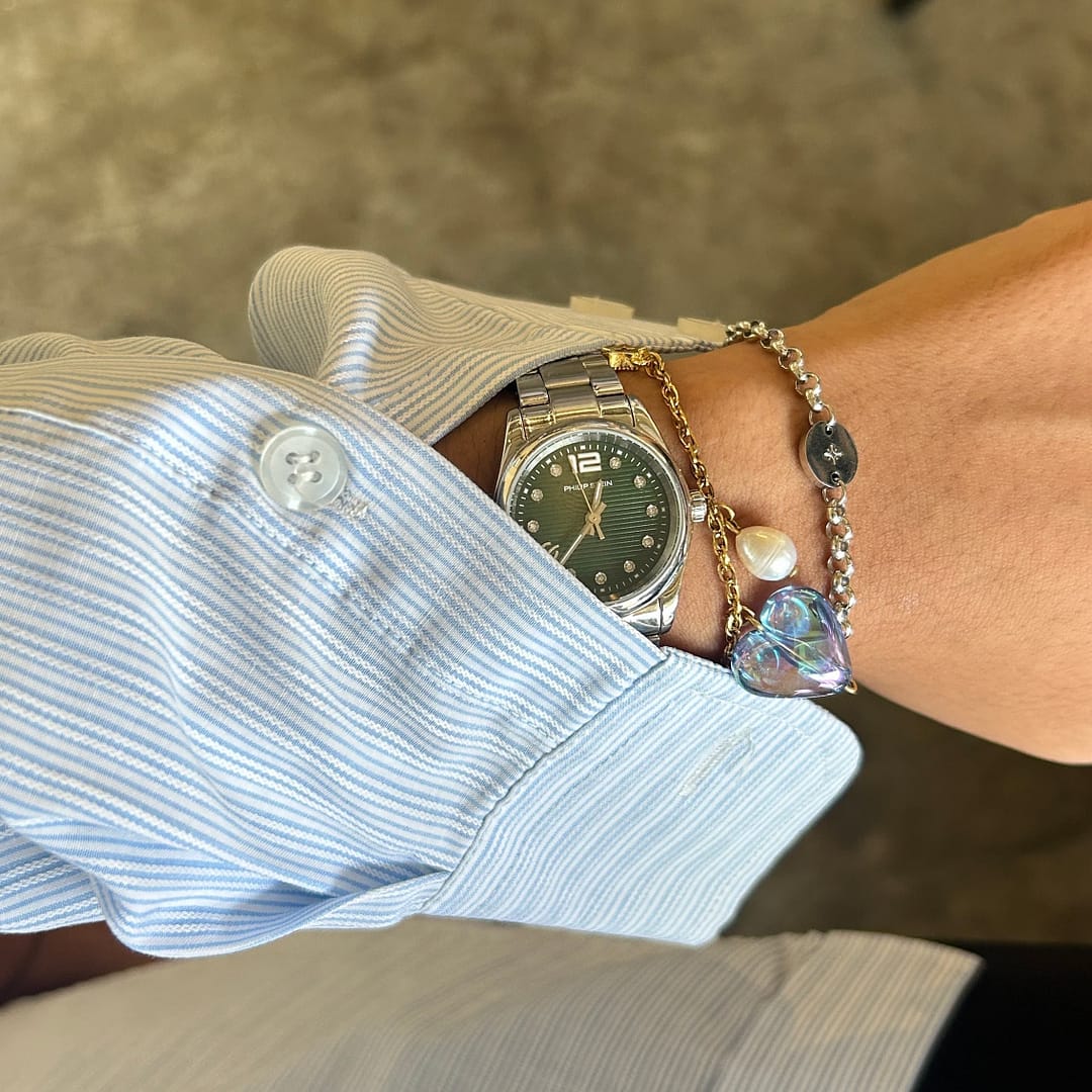 Woman in a striped shirt showcases a stylish watch and two beaded bracelets on their wrist