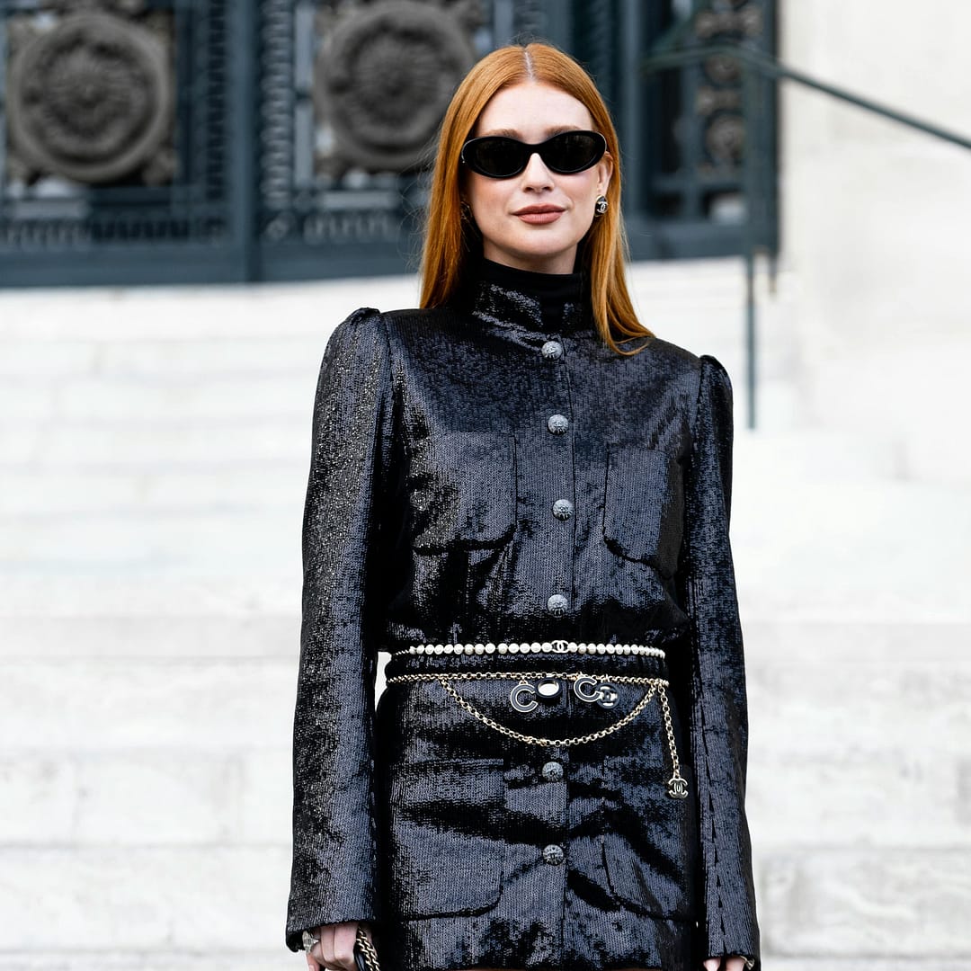 Woman looking very chic in a black sequined outfit and stylish sunglasses, holds a small black handbag while posing confidently on steps before ornate metal doors