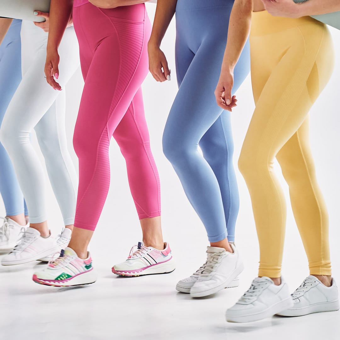 A group of people in vibrant leggings and white sneakers, clutching rolled yoga mats, stands confidently against a pristine white background