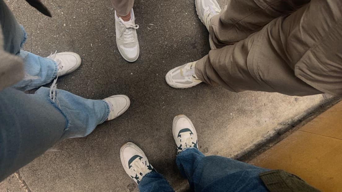 Four women stand in a circle on a concrete surface. Each showcases their unique style with different white sneakers