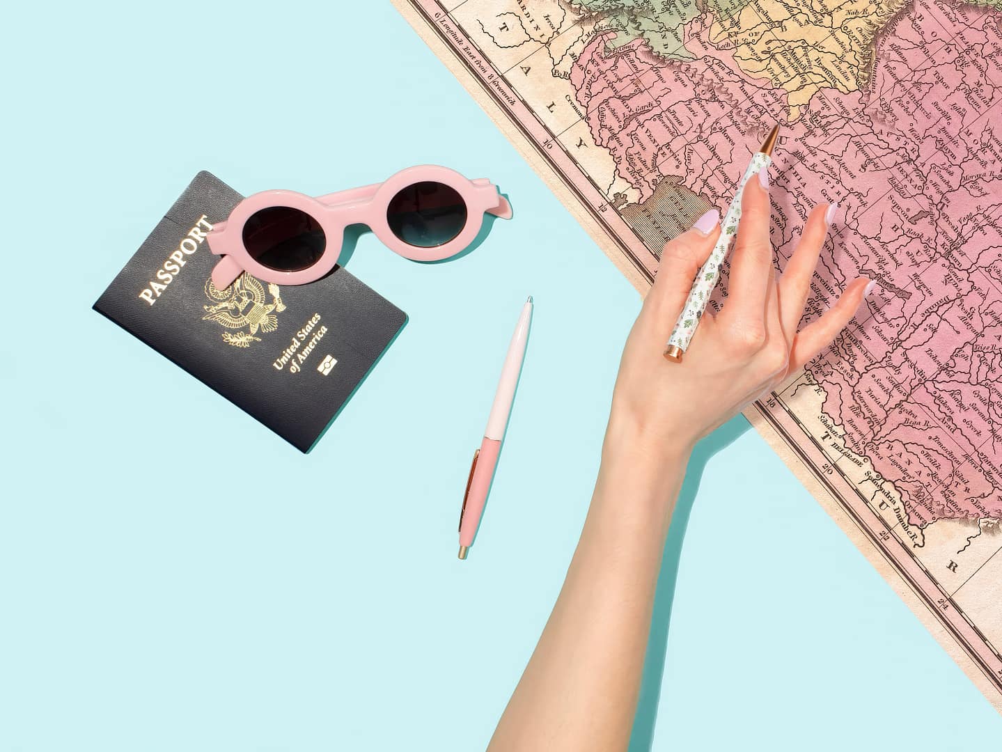 A woman's hand holding a pink pen and a passport placed on a map