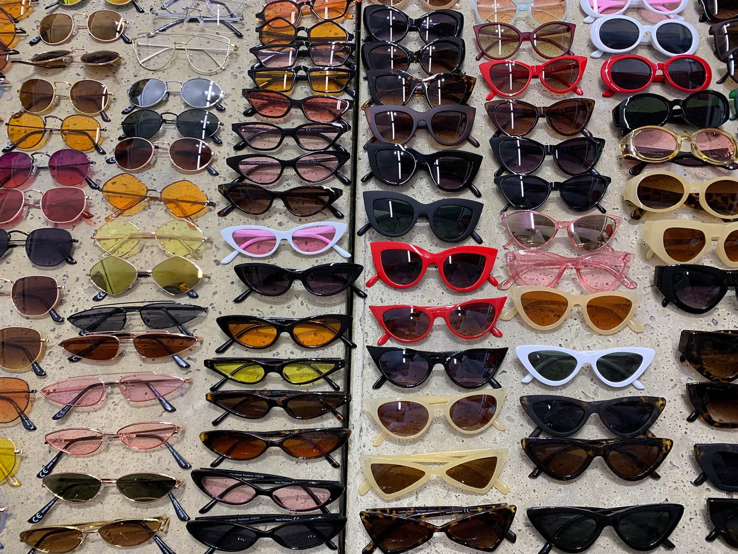 Various sunglasses with different shapes, colors, and frame styles arranged in rows on a surface