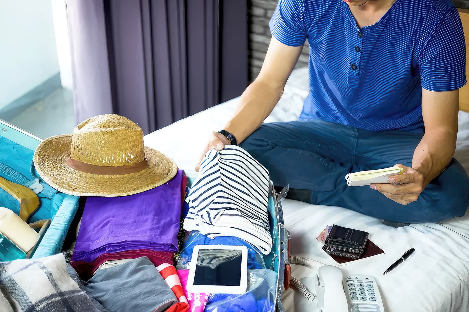 A man sitting on a bed with a suitcase full of clothes