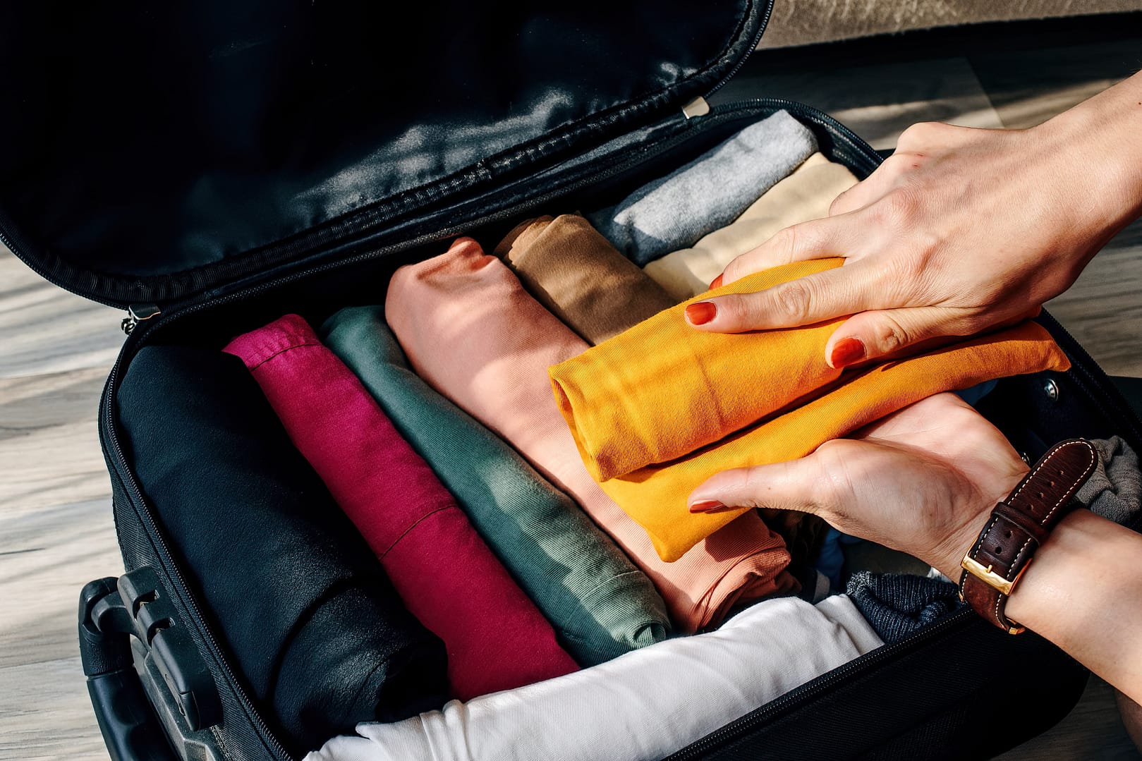 A hand holding and rolling an orange t-shirt to pack in a travel luggage suitcase