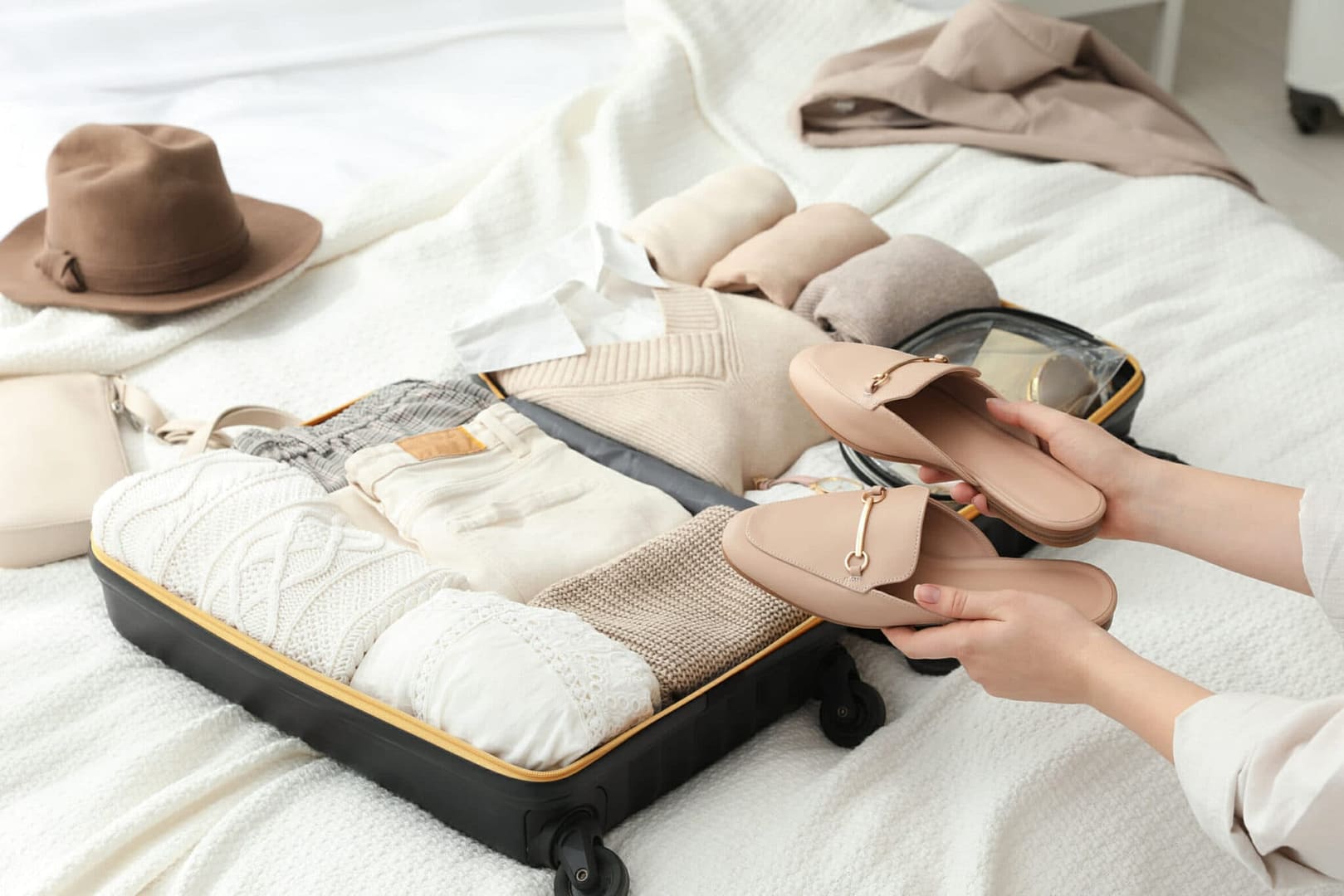 Woman holding fashionable shoes near open suitcase on bed