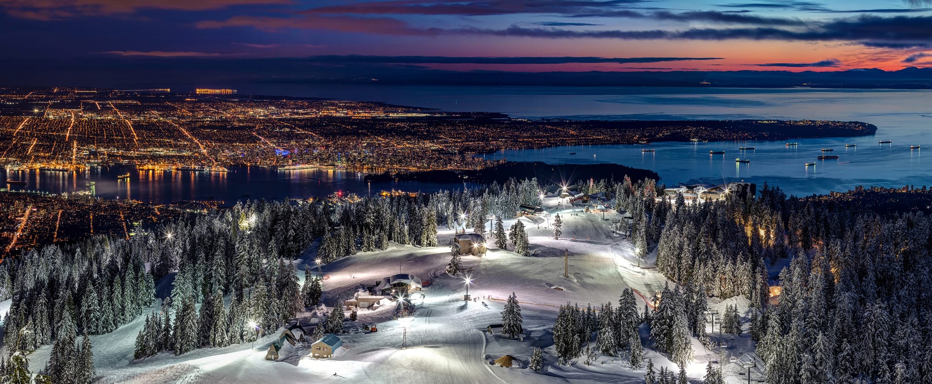 Skiing on the illuminated ski slopes of Grouse Mountain with a view of Vancouver City at dusk