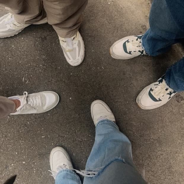 Four women stand in a circle on a concrete surface. Each showcases their unique style with different white sneakers